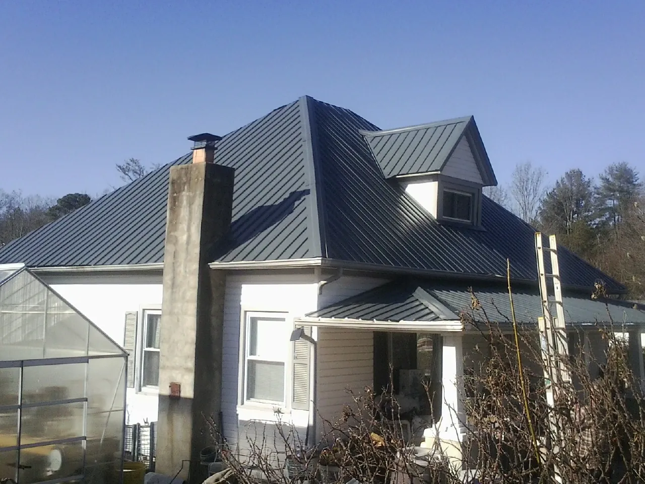 Dark blue standing seam metal roof on a white farmhouse with dormer — Slate & Tile Roof Repair by Roofing Brothers in Erie