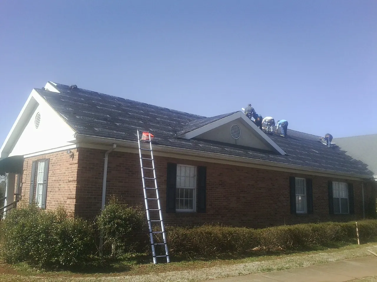 Crew tearing shingles off a brick ranch roof with a ladder set — Emergency Roof Repair work by our crew in Erie