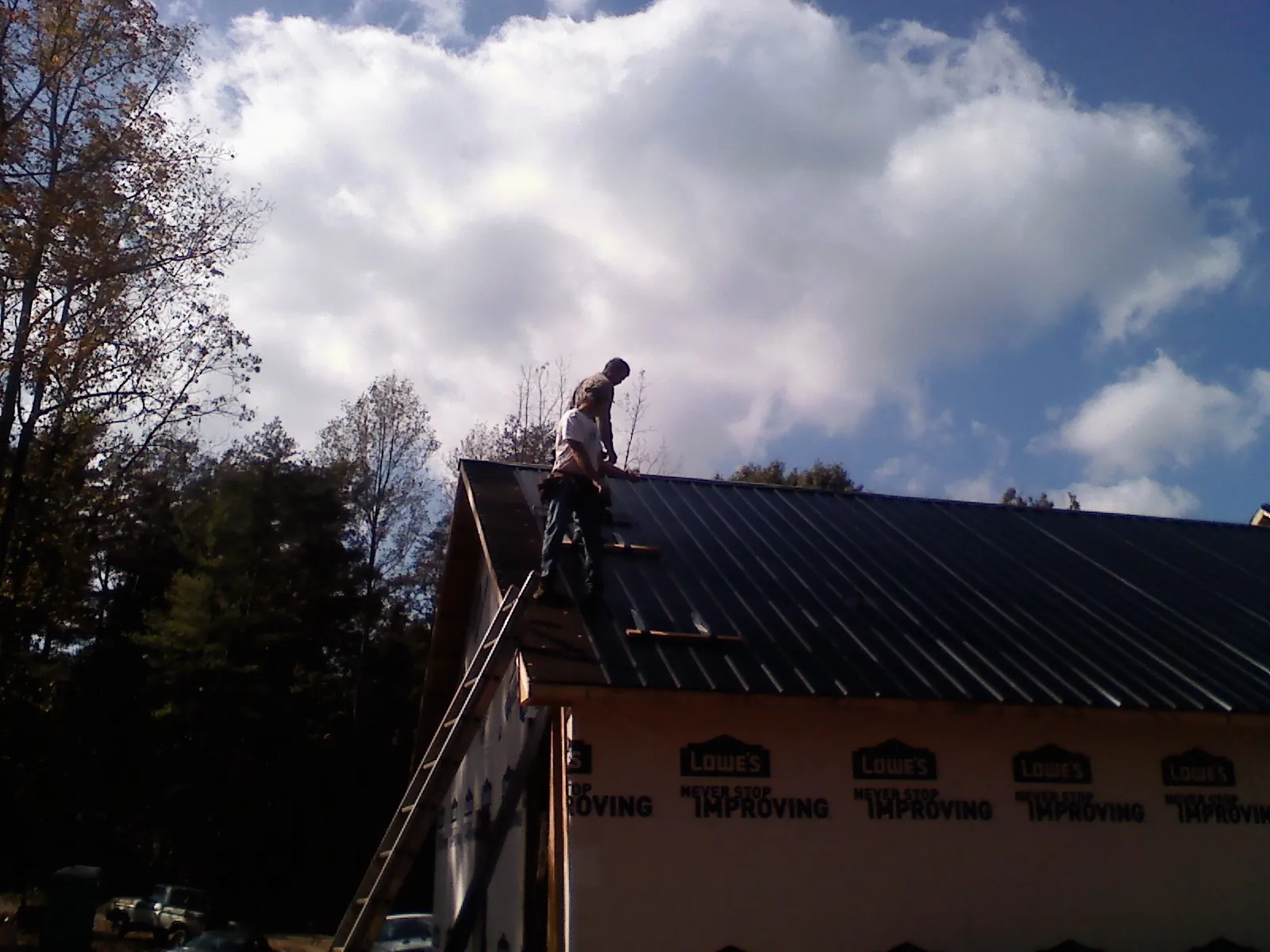 Roofer fastening dark metal panels high against a cloudy sky, from a Roof Inspection job in Erie